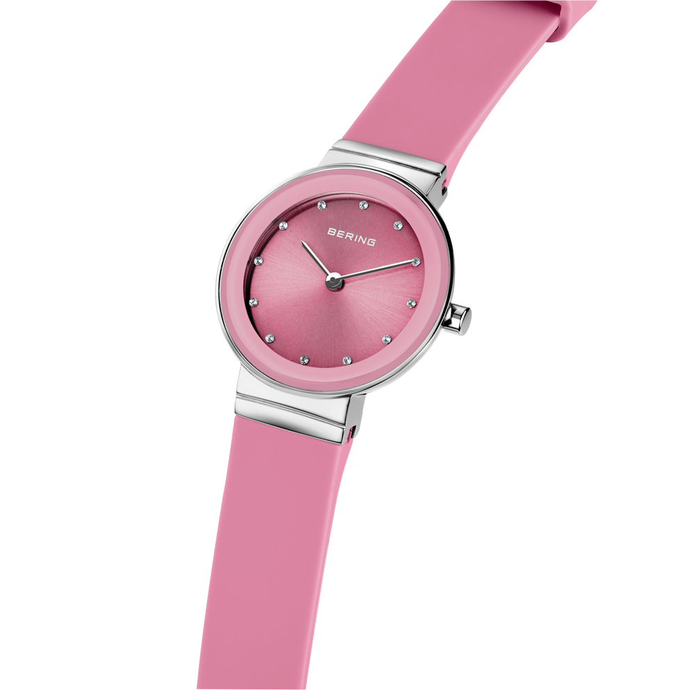 Pink wristwatch with round dial and silicone strap, angled view showing metal case connector.