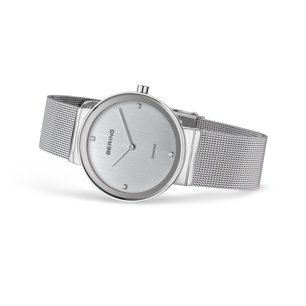 Montre-bracelet minimaliste argentée avec cadran rond et bracelet maille acier, vue de profil.