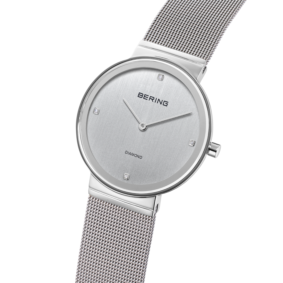 Montre ronde avec marqueurs diamants, vue en angle montrant le bracelet maille métallique.