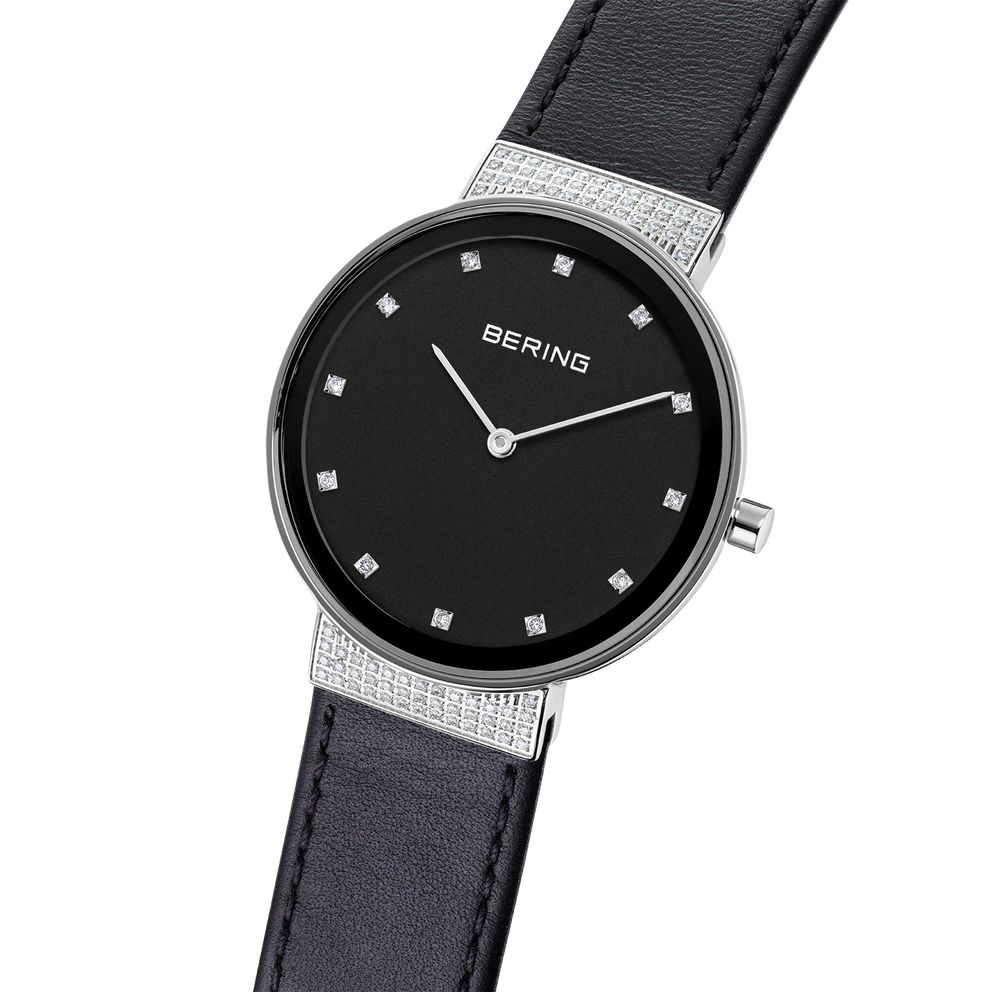 BERING horloge met zwarte wijzerplaat, zilveren lunette, diamantmarkeringen en leren band in schuinhoek.