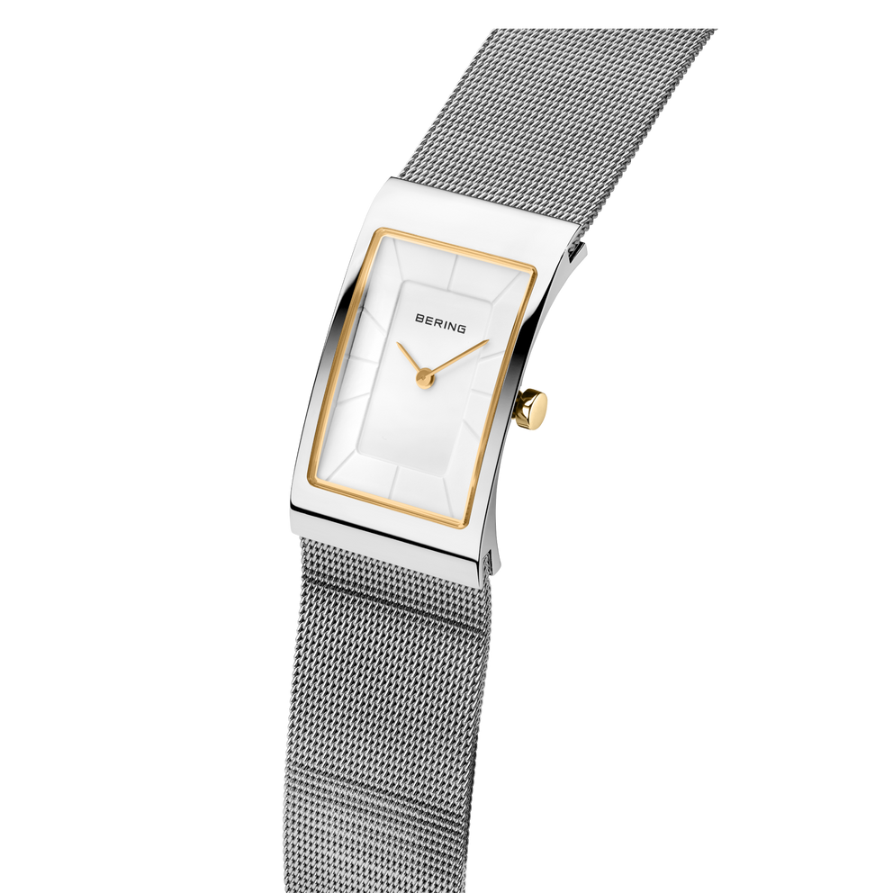 Reloj BERING visto en ángulo: esfera rectangular blanca con bisel dorado, pulsera malla acero con acabado texturado.