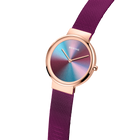 Reloj BERING Anniversary en ángulo con caja oro rosa, esfera iridiscente degradada y correa malla púrpura.