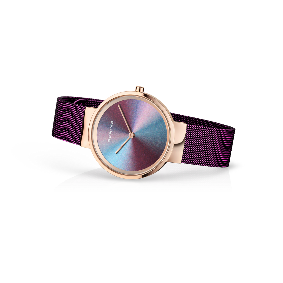 Reloj BERING Anniversary en vista 3/4 con caja oro rosa, esfera iridiscente y correa malla púrpura.