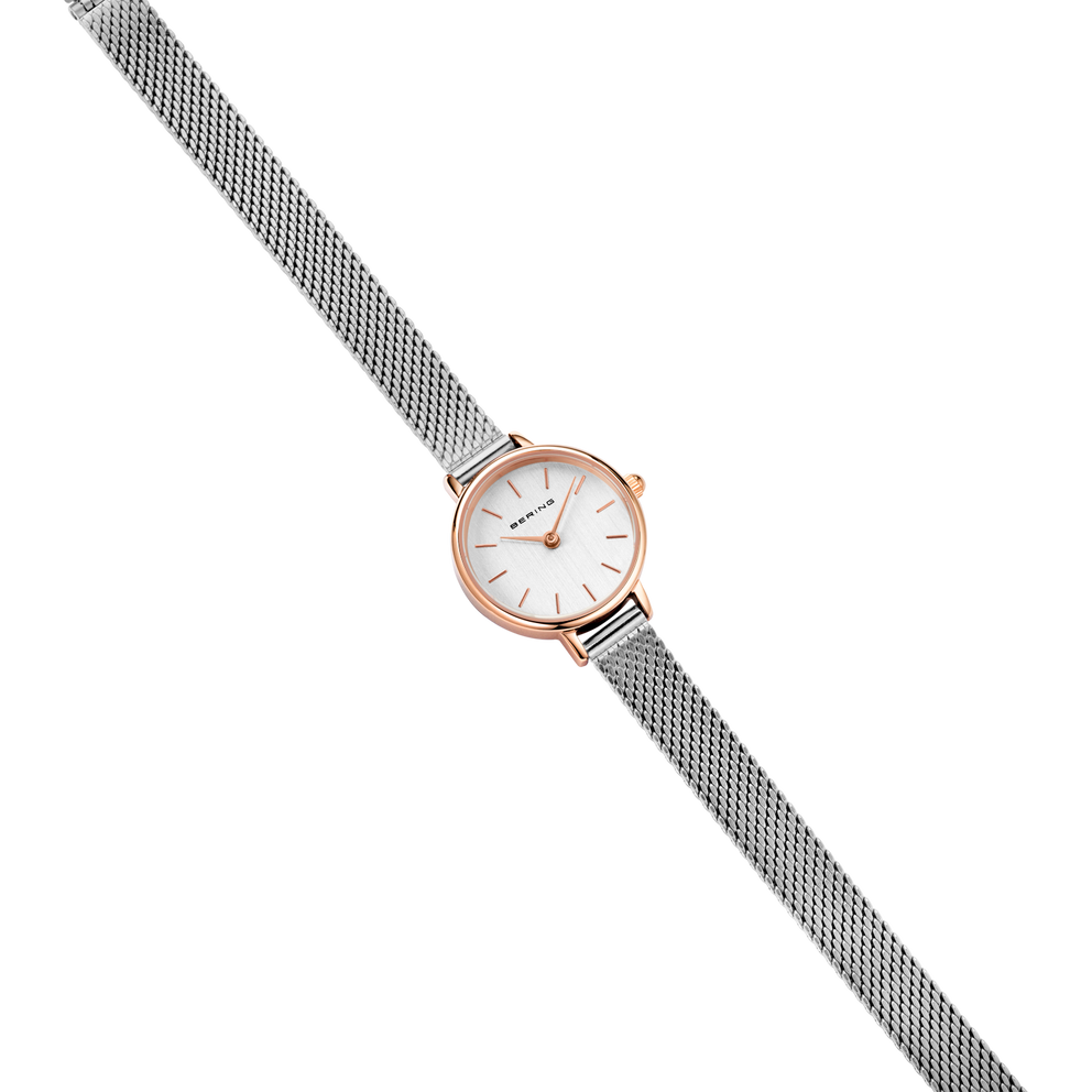 Reloj de oro rosado con esfera blanca y pulsera malla gris, fotografiado en ángulo