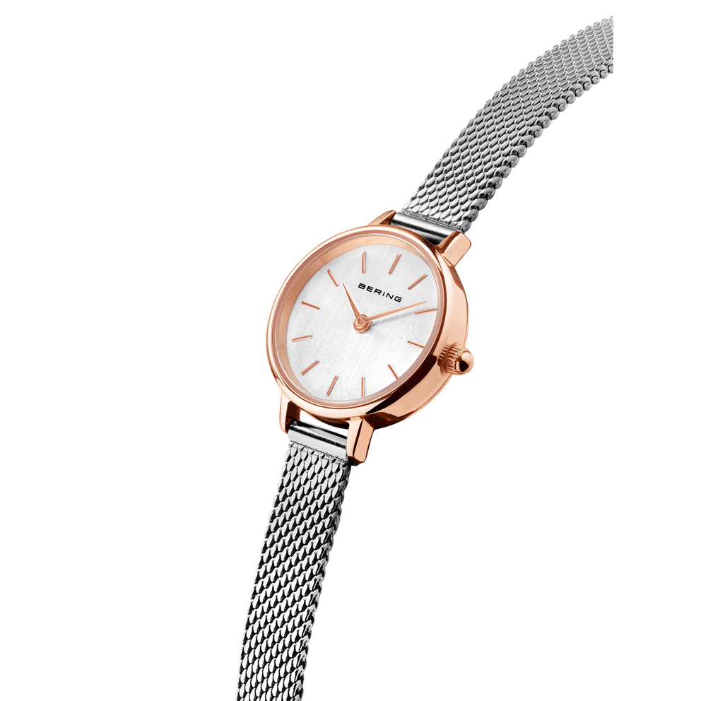 Reloj BERING con caja oro rosa, esfera blanca y correa malla acero, fotografiado desde el lateral.