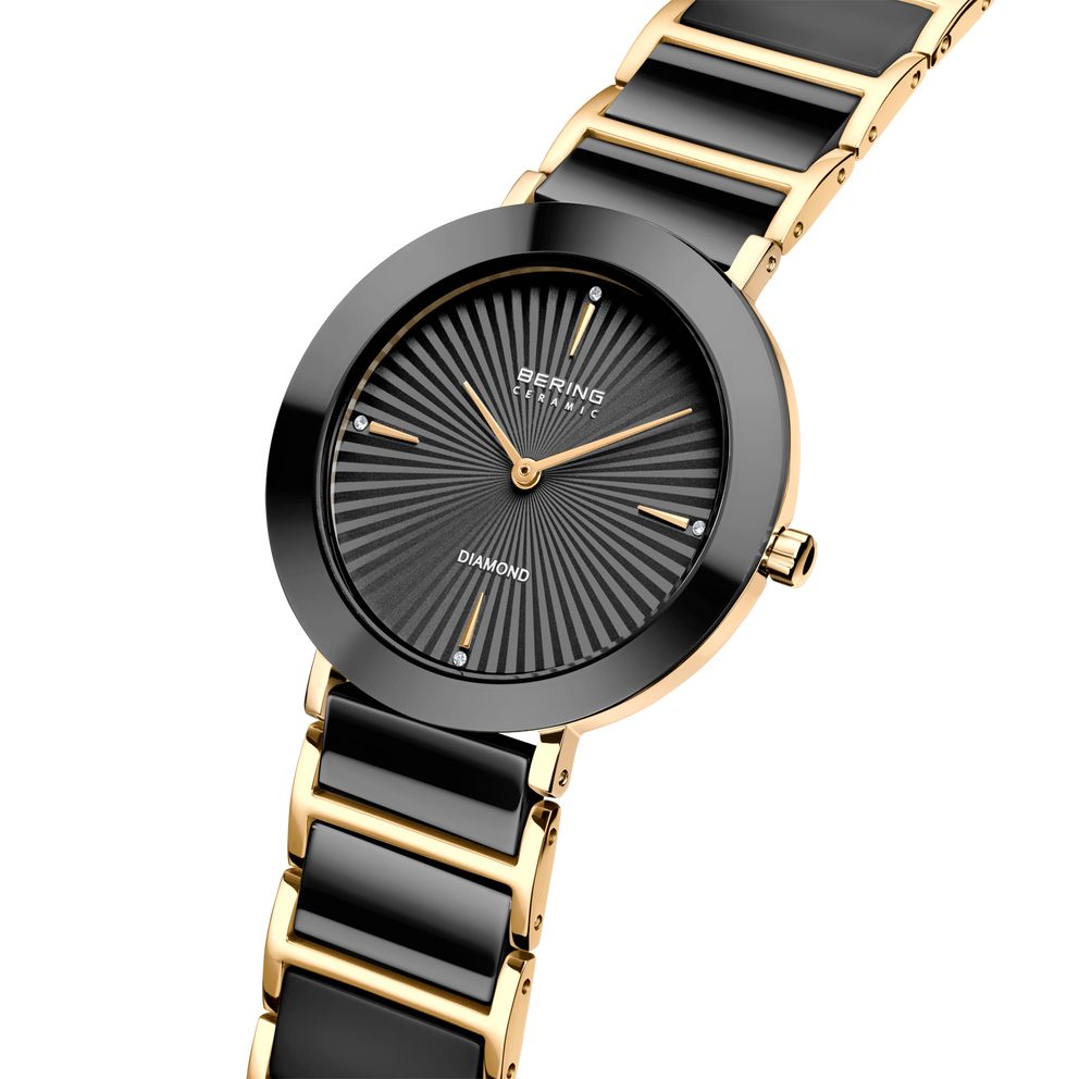 Orologio da polso BERING bicolore con quadrante raggiato scuro e bracciale a maglie oro e nero.