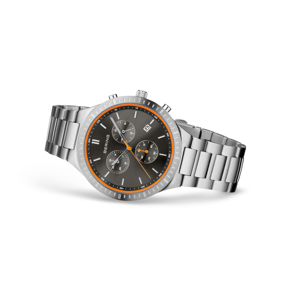Steel chronograph watch with black dial, orange bezel, and three sub-dials, shown at three-quarter angle.