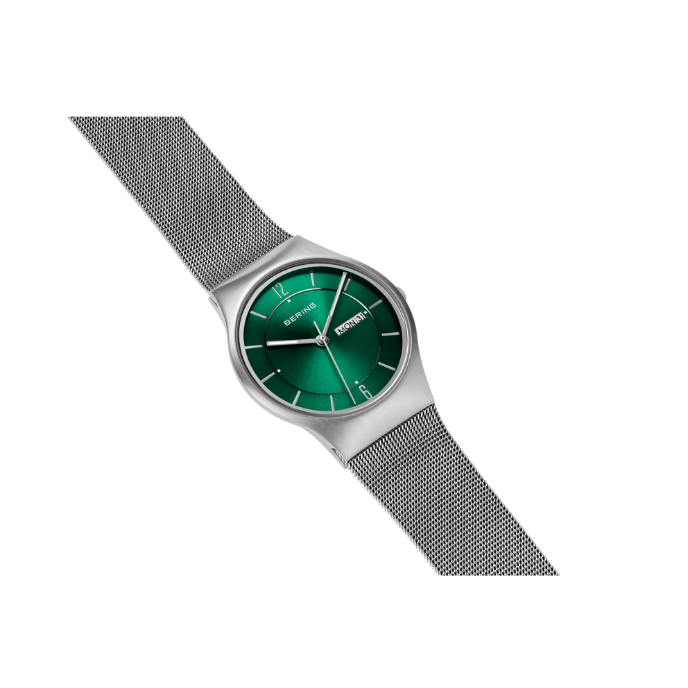 Round wristwatch with green dial, silver case, and gray mesh band, tilted view