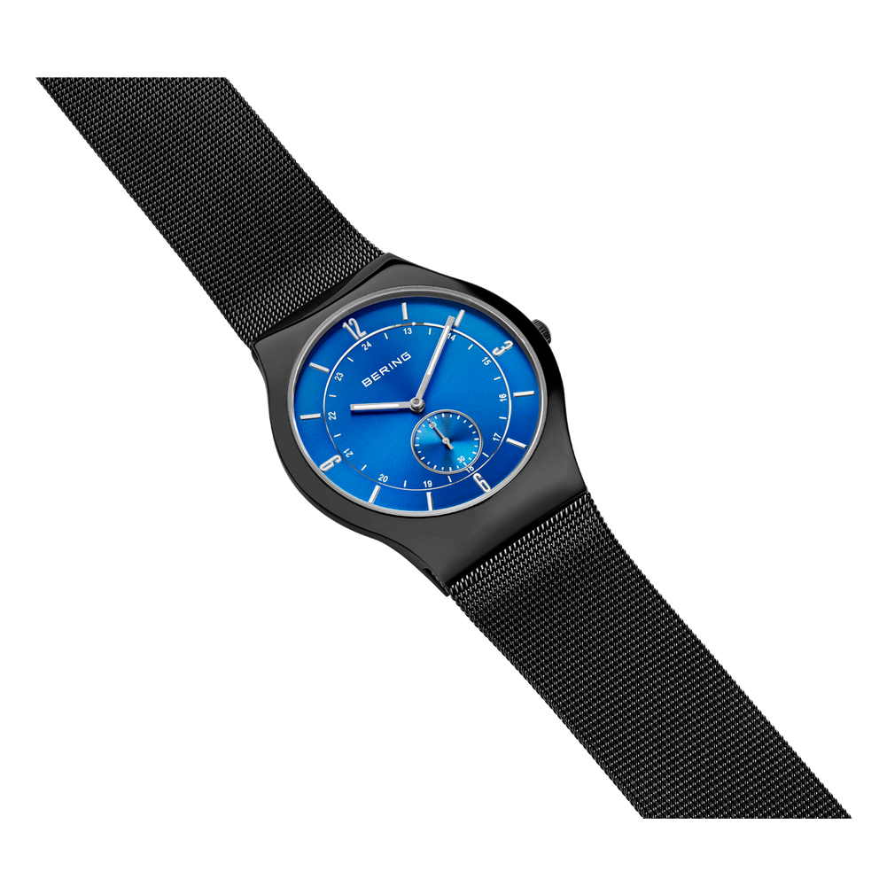 Black round watch with bright blue dial and white markers, black mesh band, shown at three-quarter angle