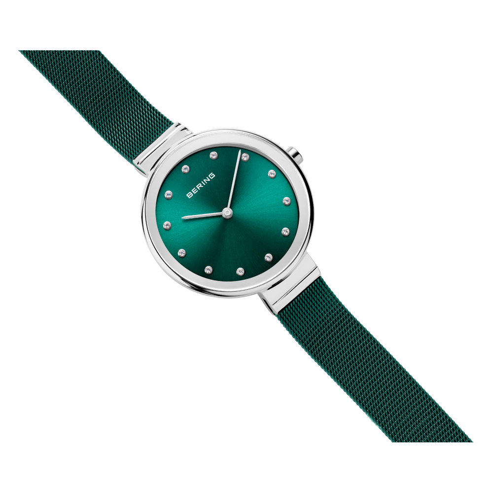 Wristwatch with teal dial, white hour markers, silver case, and textured fabric strap angled across frame.