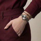 Rose-gold watch with mesh band worn on wrist with burgundy jacket