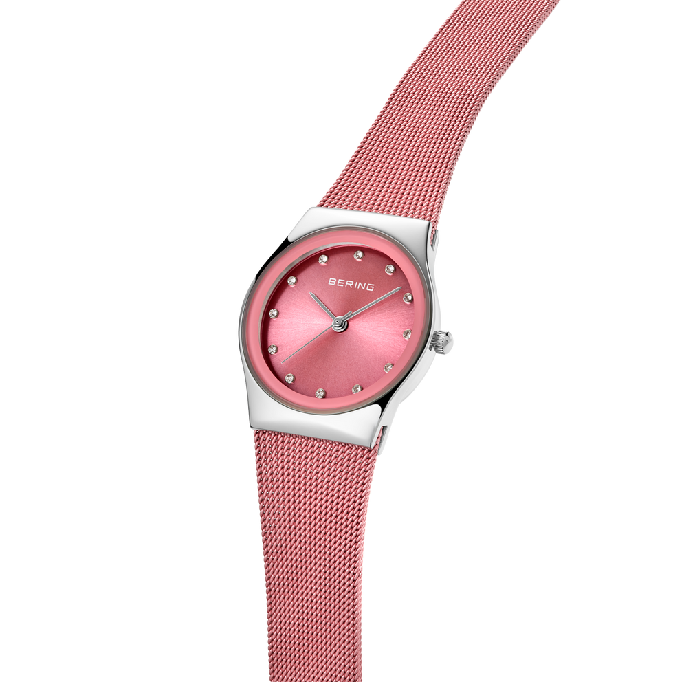 Wristwatch with rose-pink dial, silver case, and matching rose-pink mesh band draped across the watch case.