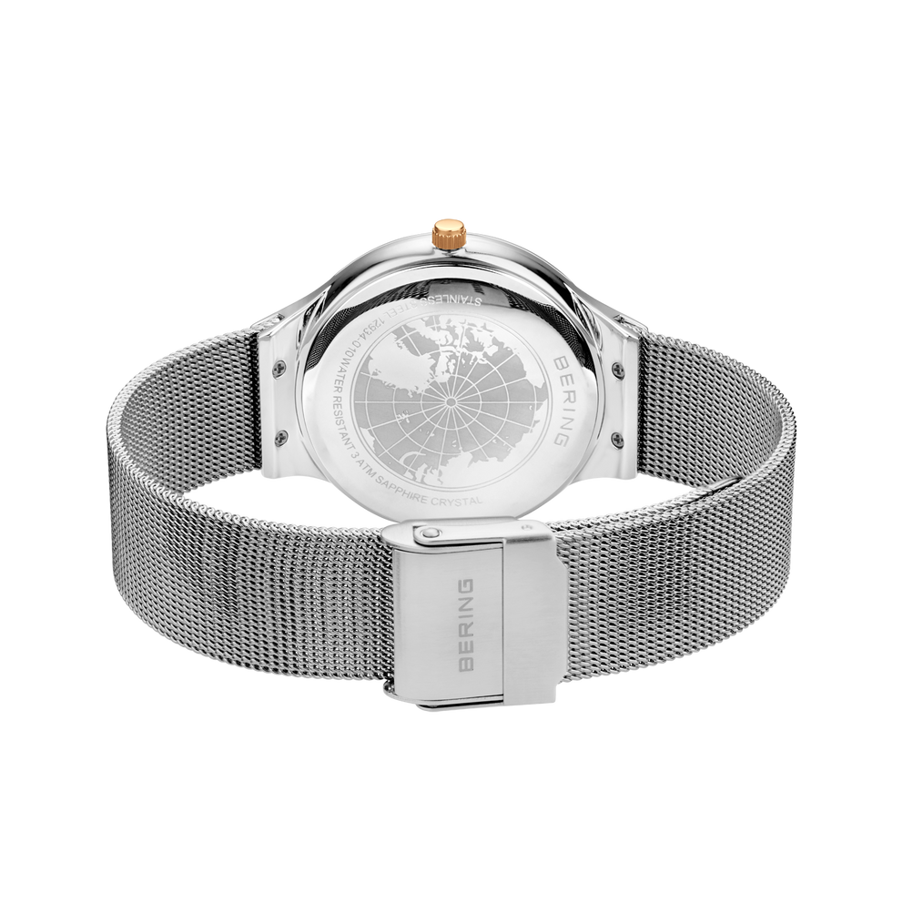 Verso de la montre avec design de globe, bracelet maille argentée, fermoir métallique visible.