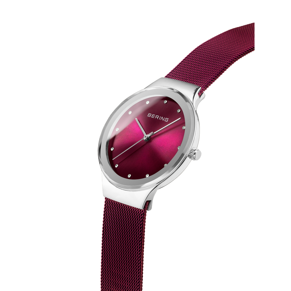 Horloge met bordeauxrood gradatie wijzerplaat en bijpassend mesh-bandje, in schuine hoek op witte achtergrond.