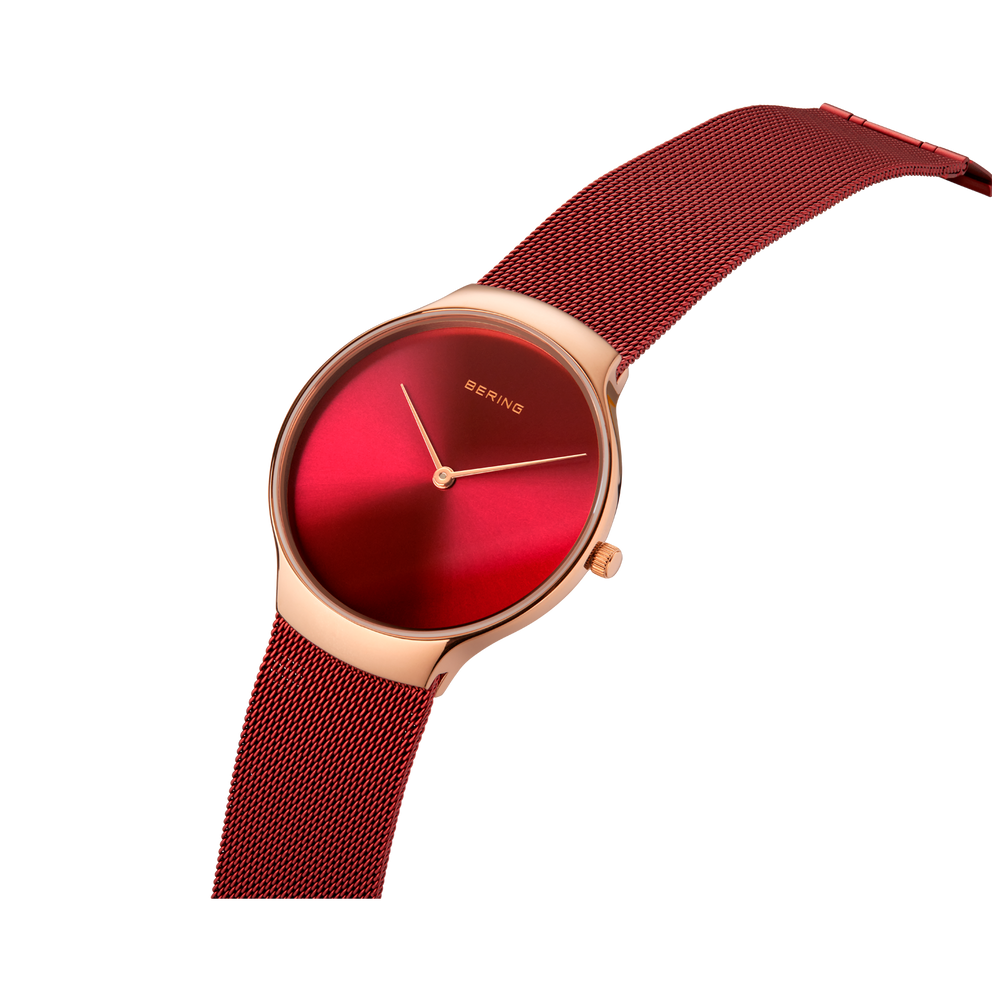Wristwatch with rose gold case, deep red dial, and burgundy mesh band shown at an angle.