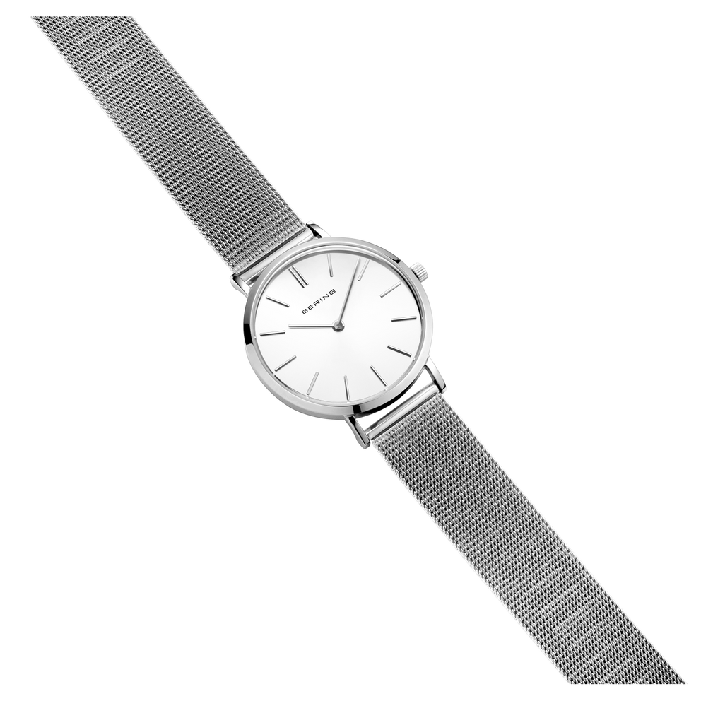 Minimalistische Armbanduhr mit silbernem Gehäuse, weißem Zifferblatt und grauem Mesh-Metallband, diagonal dargestellt.