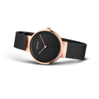Wristwatch with rose gold case, black mesh strap, and minimalist black dial with three hands.