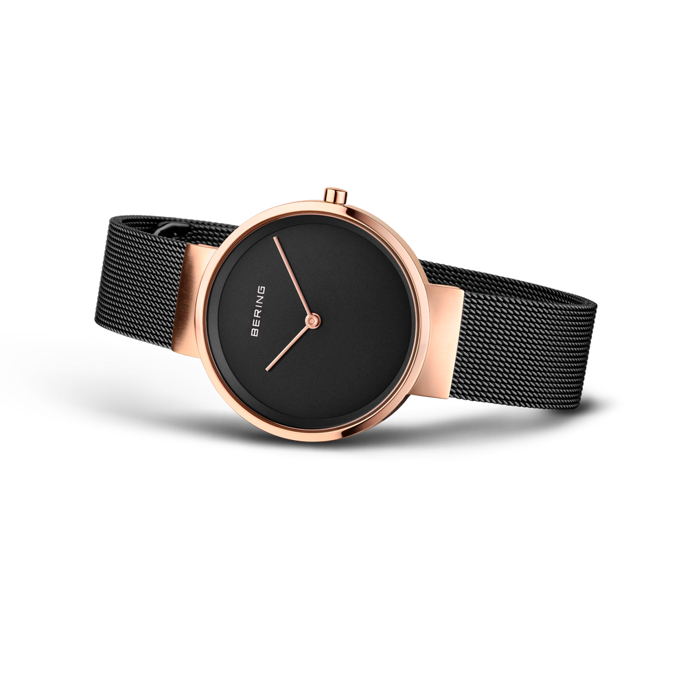Wristwatch with rose gold case, black mesh strap, and minimalist black dial with three hands.