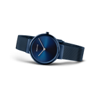 Reloj de pulsera con esfera azul redonda, manecillas delgadas, pulsera de malla oscura, vista en ángulo.