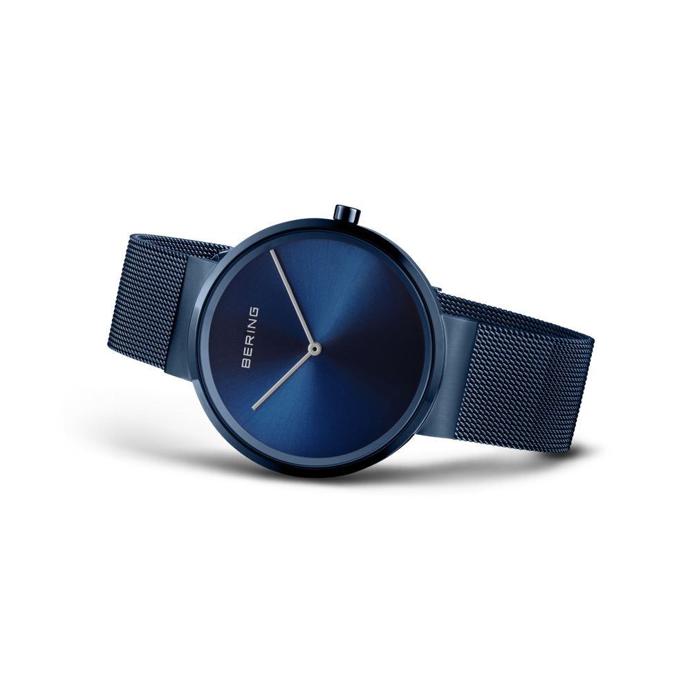 Reloj BERING azul oscuro con esfera minimalista y correa malla metálica, vista frontal en ángulo.