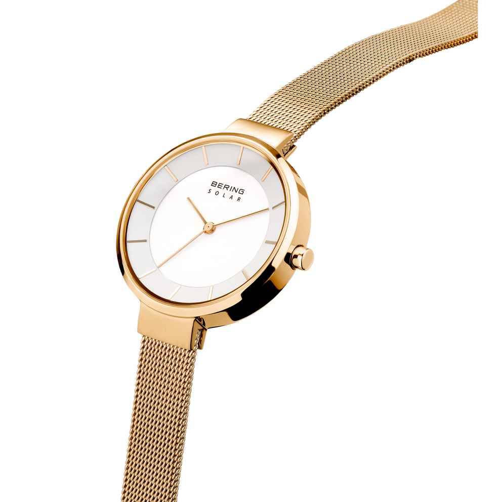 Round watch in champagne gold with white dial and textured mesh band, shown at three-quarter view.