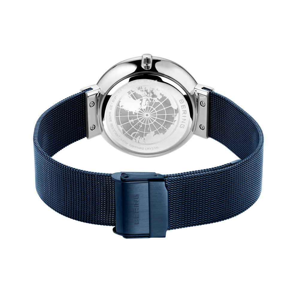 Montre affichée de face avec bracelet mailles bleu marine et boucle assortie; cadran avec motif globe et lunette chromée.