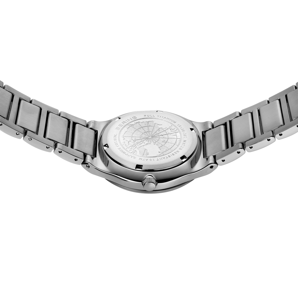 Reloj fotografiado desde atrás con pulsera de acero y fondo visible