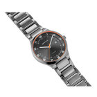 Reloj con caja gris, bisel oro rosa, esfera negra con marcadores de horas y pulsera de metal gris, vista en ángulo.