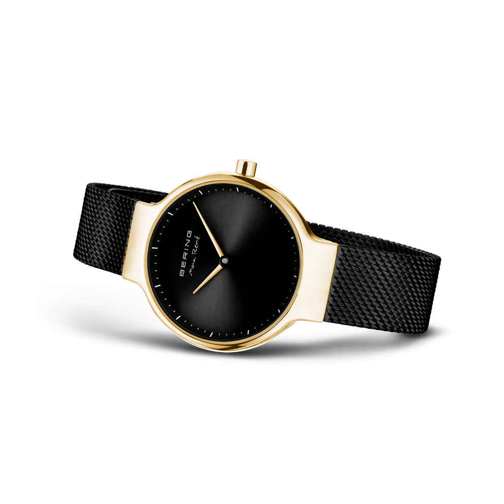 Wristwatch with black dial, white hands, gold case, and black mesh band, shown at angle.