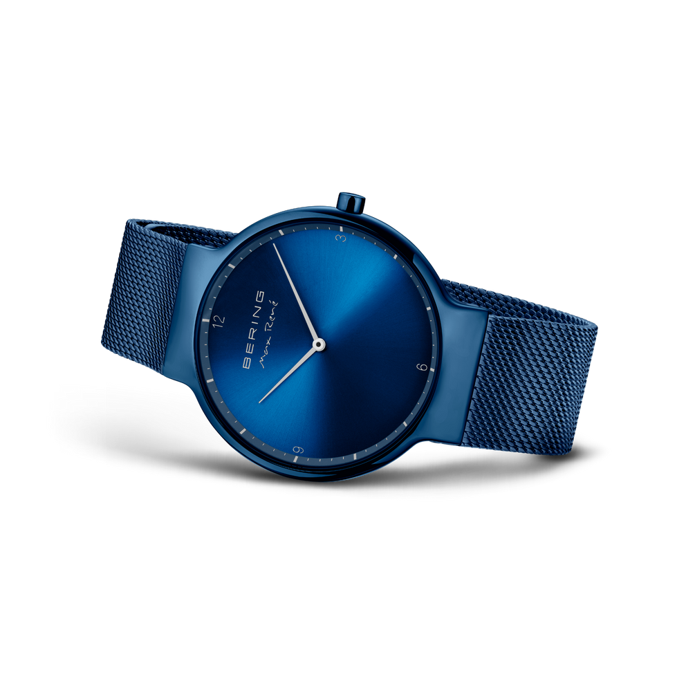 Armbåndsur i tre-kvarts vinkel, blåt mesh-bånd, mørkeblå urskive med hvide minimalistische markeringer og visere.
