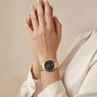 Orologio minimalista con quadrante nero e cinturino in metallo color oro indossato al polso
