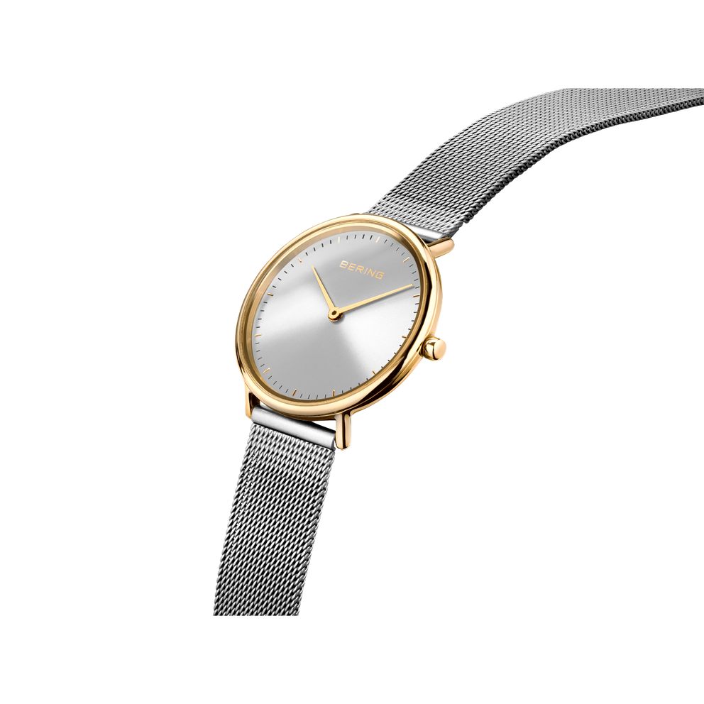 BERING horloge met goudkleurige kast, zilveren wijzerplaat en stalen mesh-band, gefotografeerd onder hoek.