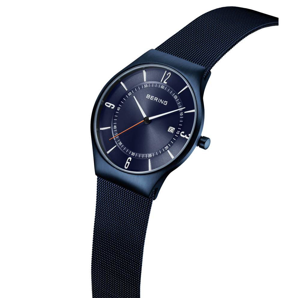 Dark blue BERING watch displayed at angle, showing navy mesh band and dial with hour markers.
