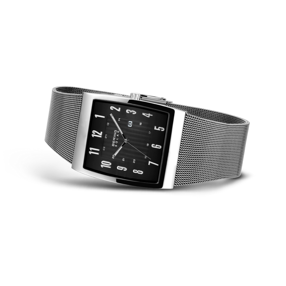 Rectangular black dial watch with white numerals and hands, silver mesh metal band, photographed at an angle.