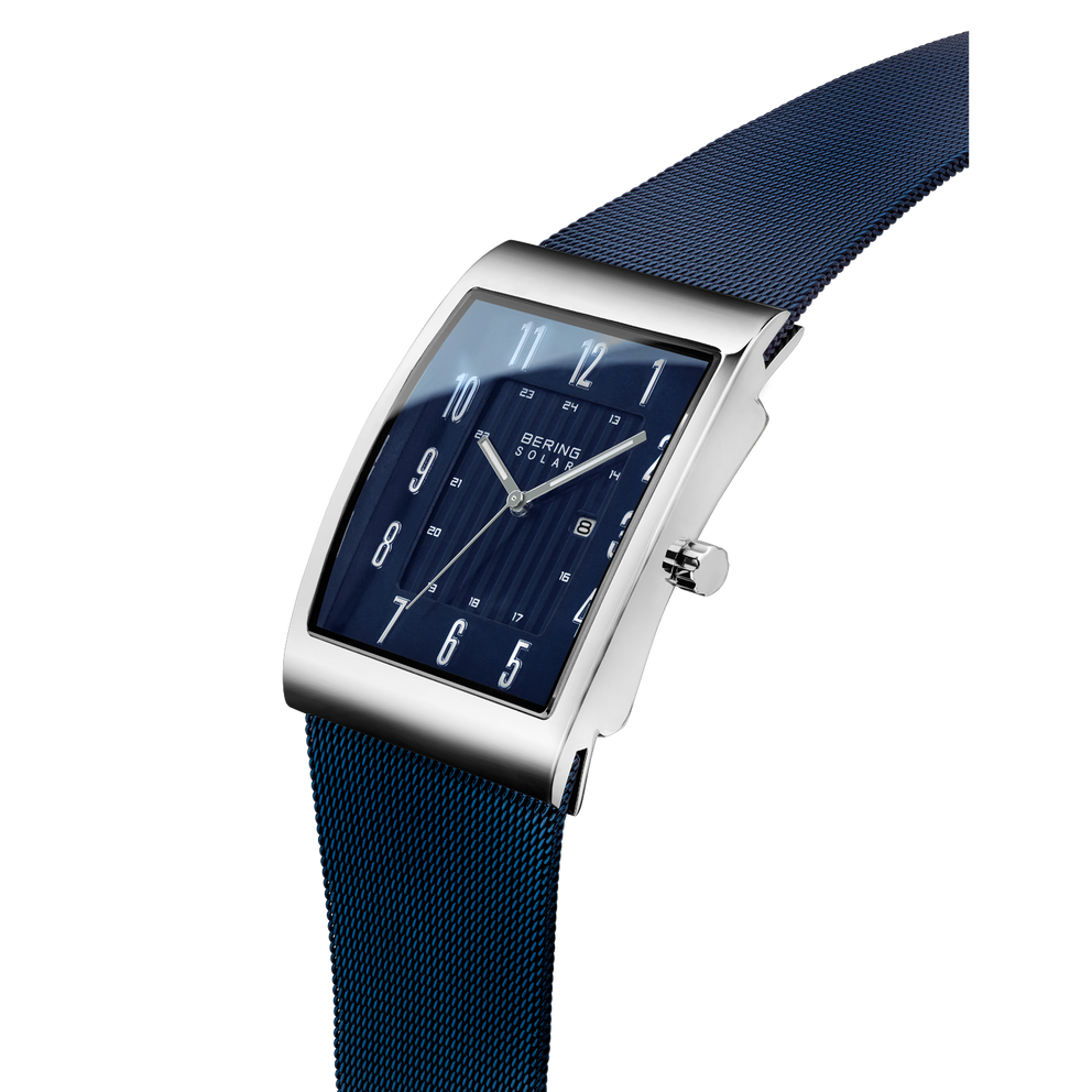 Rectangular steel watch with dark blue face and white numerals, paired with navy textile strap, shown at angle.