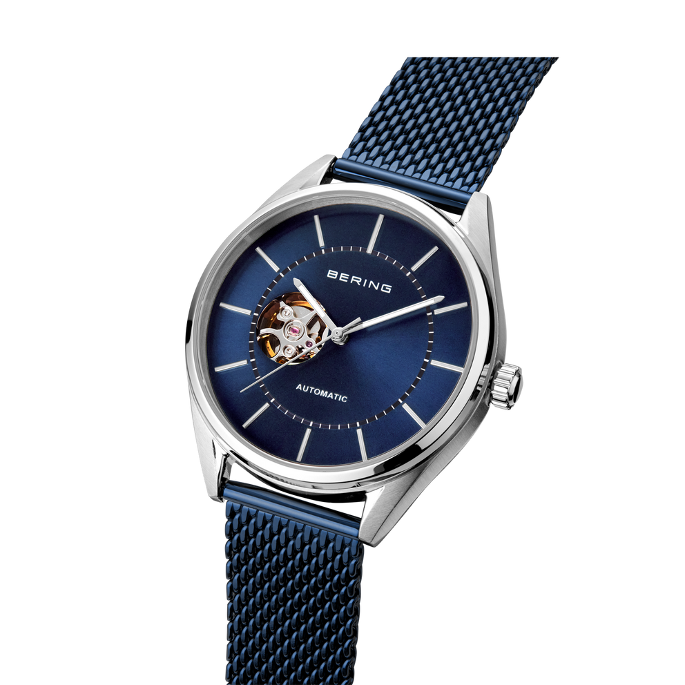 BERING automatic watch with open heart dial and blue mesh bracelet, angled product view.