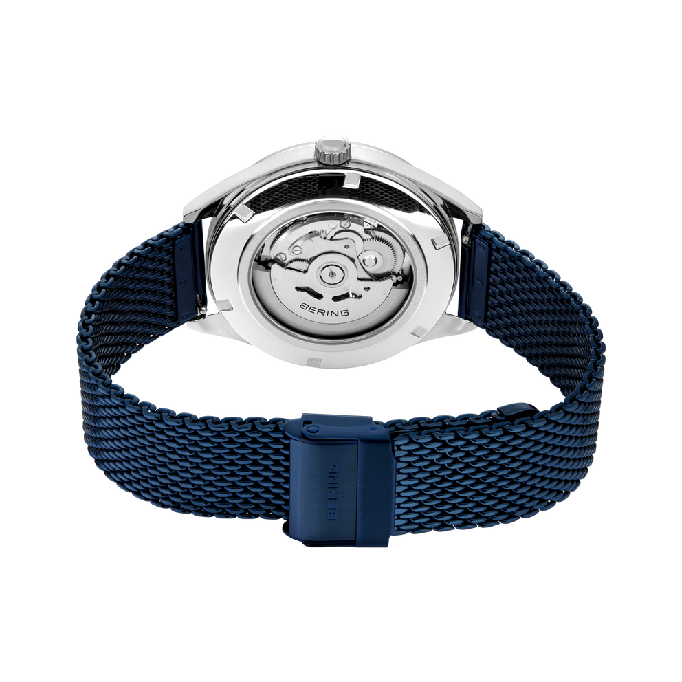 Watch caseback revealing visible movement and mechanism through transparent crystal, dark blue mesh strap with matching clasp