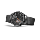 Wristwatch with round dark dial, hour markers, and open window detail; black mesh band.
