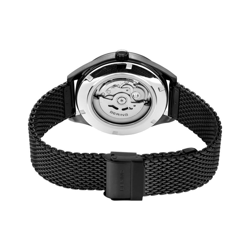 Watch shown from caseback with visible automatic movement, silver round case, and black mesh metal strap.