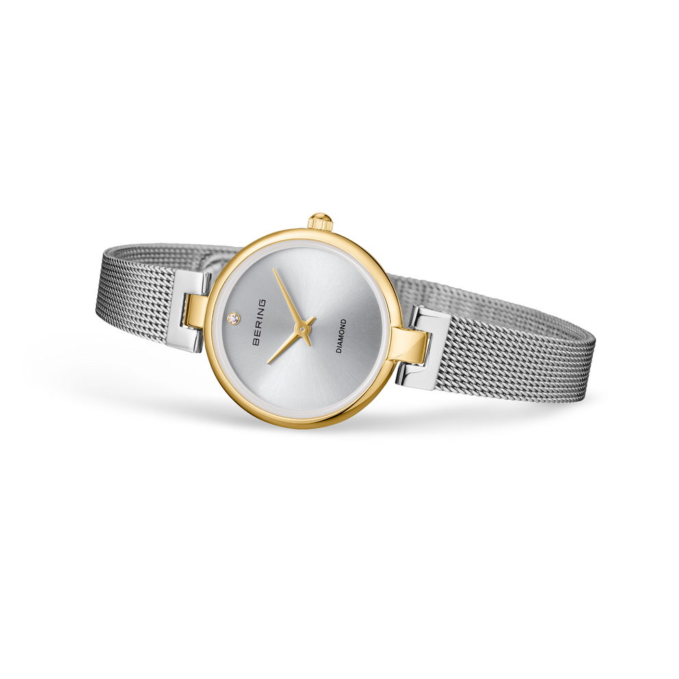 Round watch with silver dial, gold case details, and steel mesh strap, shown at an angle.