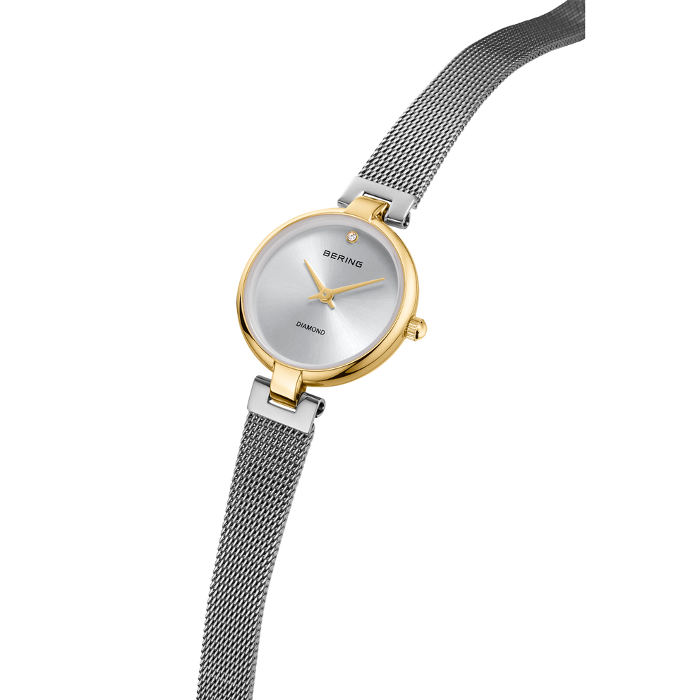 Round watch with gold case, silver dial, and dark mesh strap displayed diagonally.