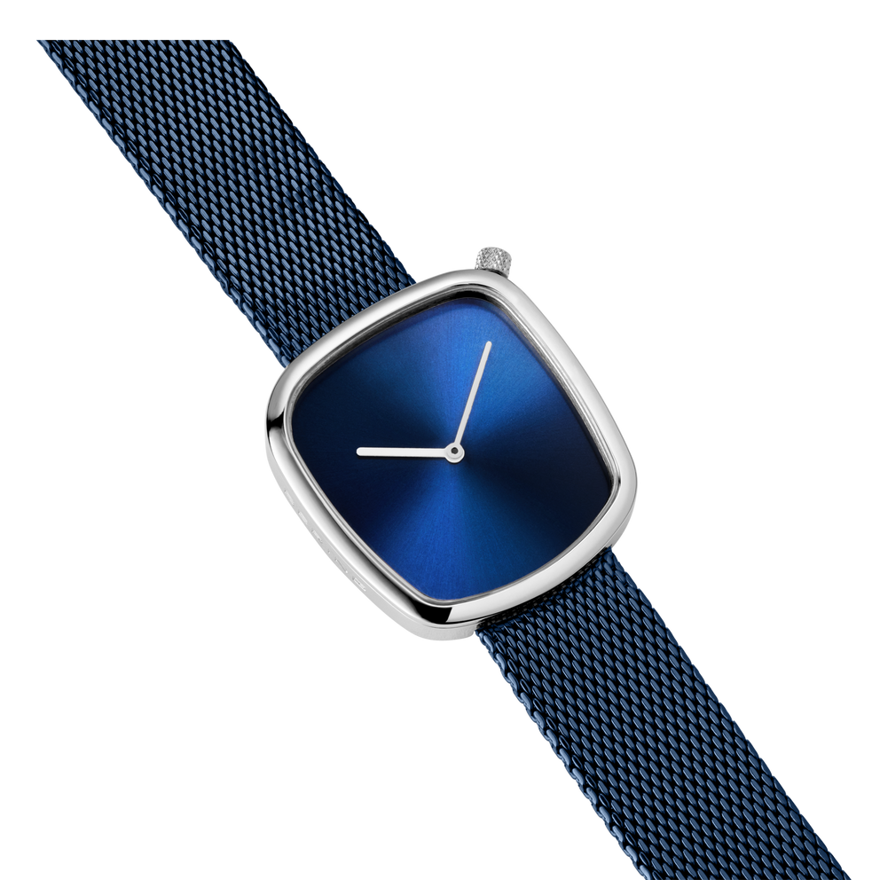Angled view of square watch case with metallic finish, dark blue textured strap, and blue dial with white hands at 3 o'clock.