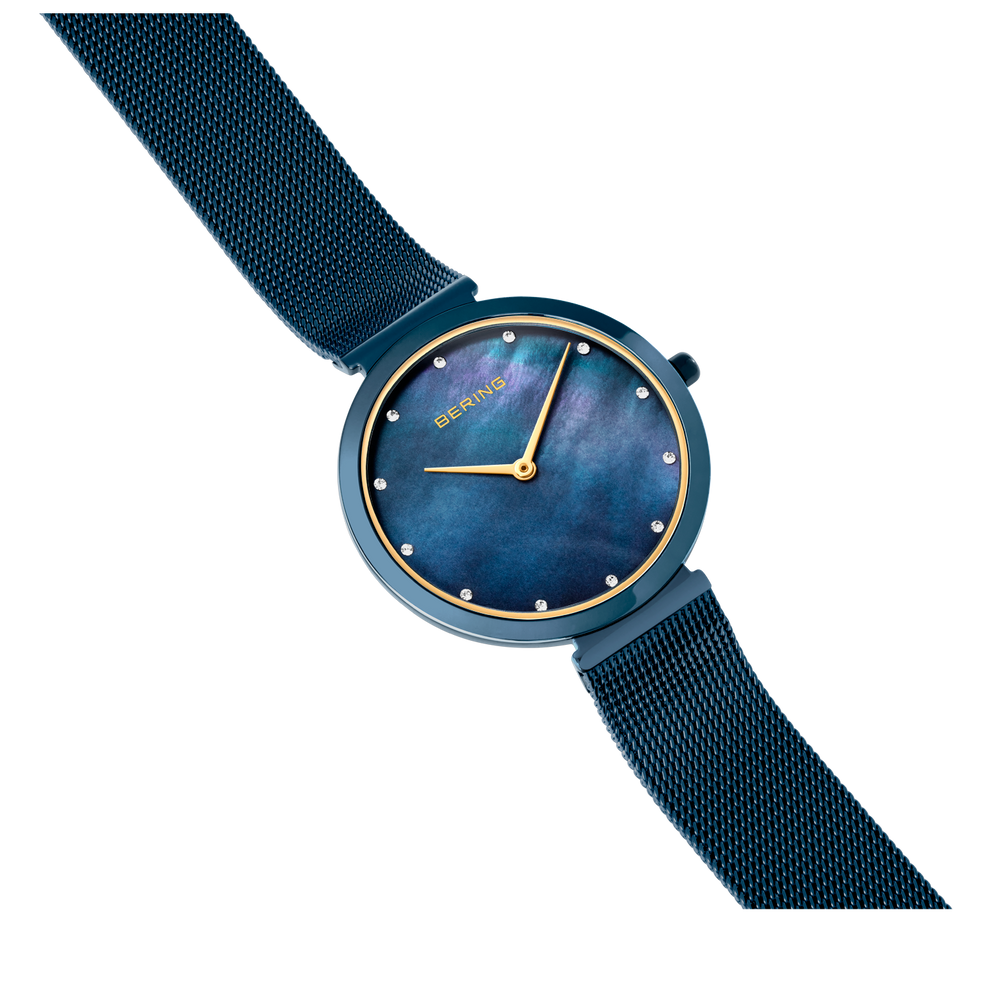 Reloj con esfera azul oscuro, índices y manecillas doradas, correa azul oscuro, vista angular sobre fondo blanco.