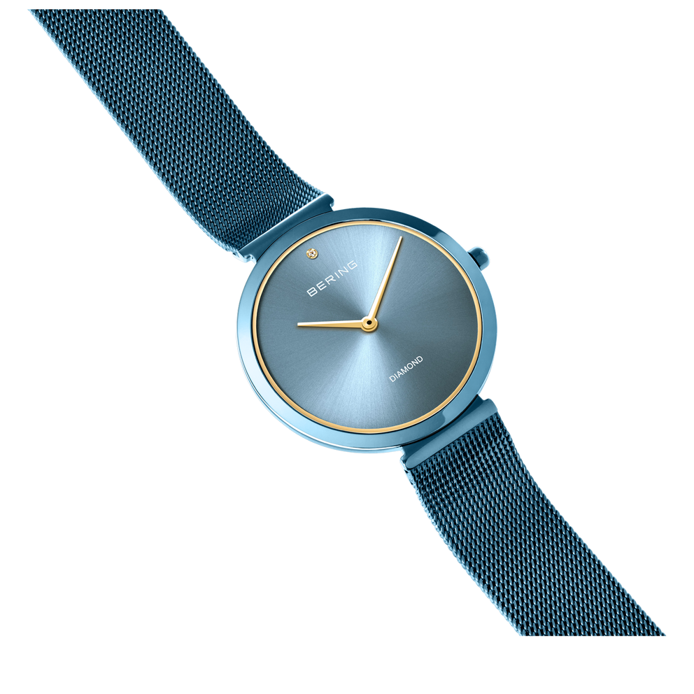 Horloge met rond blauw wijzerplaat, gouden wijzers en donkerblauwe meshband, van bovenaf fotografeerd.