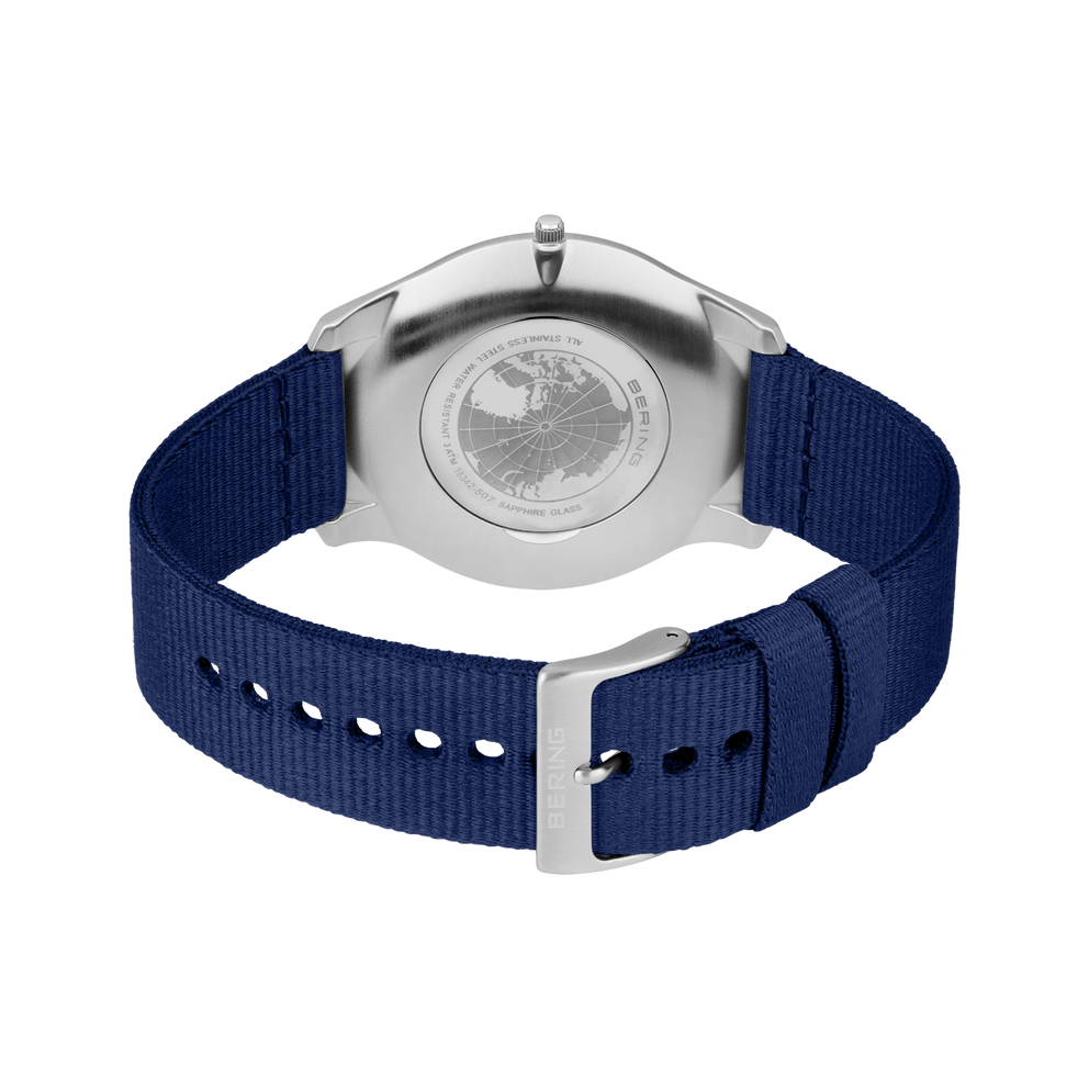 Stainless steel watch case back with dark blue textile strap and white stitching detail.