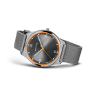 Three-quarter view of round black dial with orange bezel, Arabic numerals, and gray fabric strap.