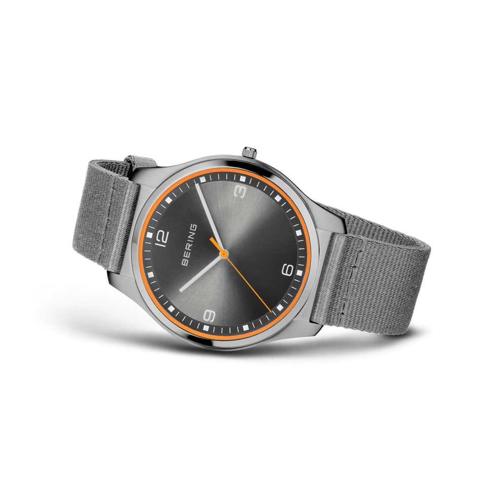 Three-quarter view of round black dial with orange bezel, Arabic numerals, and gray fabric strap.