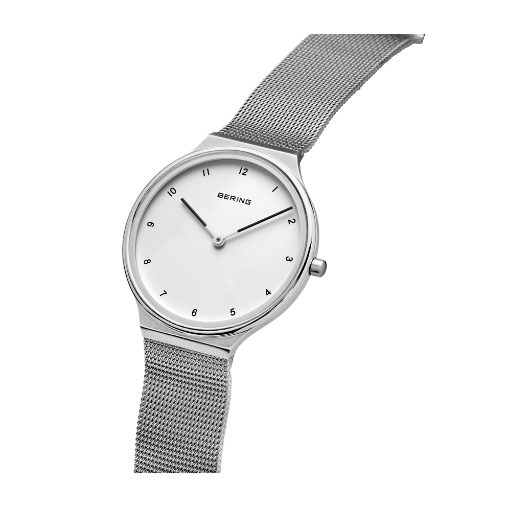 Horloge met crèmekleurige wijzerplaat, uurmarkeringen en zilveren mesh-band, schuin gefotografeerd.