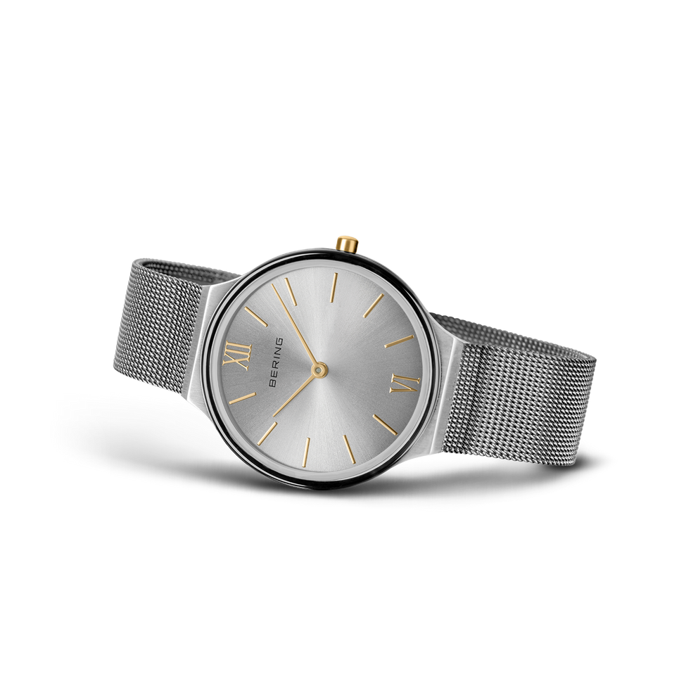Round gray dial with silver hour markers and gold hands. Mesh metal band extending from both sides.