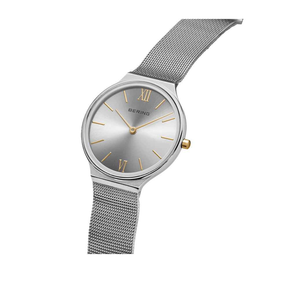 Silver round watch with dark dial, Roman numerals, and mesh metal strap, angled view.